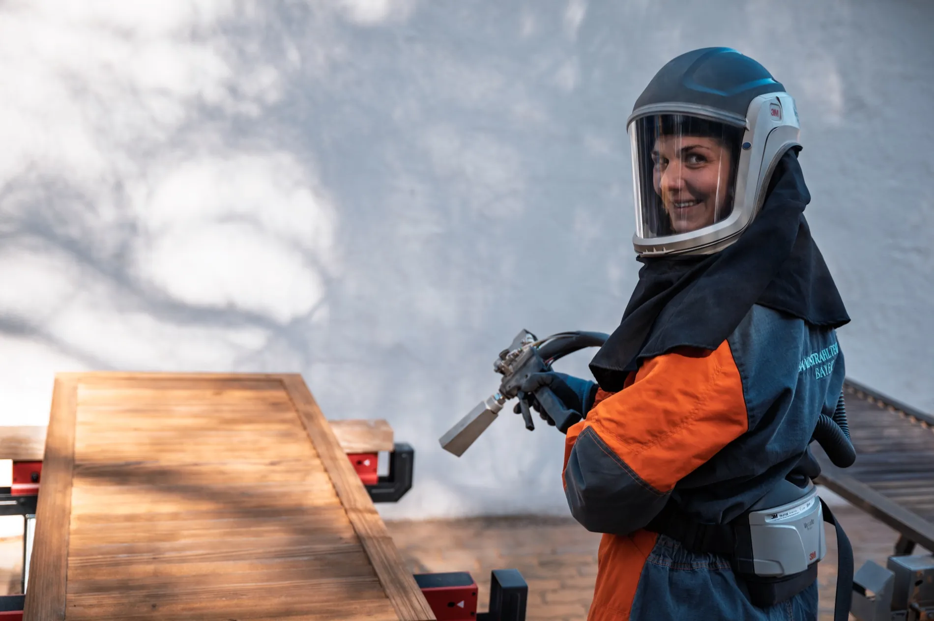 Manuela Paulus strahlt mit Schutzhelm eine Holzplatte ab